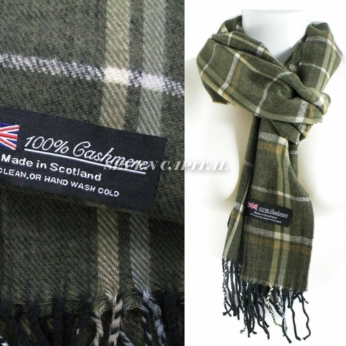 An olive green and beige plaid cashmere scarf with black fringe, shown both as a close-up of the fabric and label and as a styled wrap on a white mannequin torso. A black woven label reads '100% Cashmere Made in Scotland'.