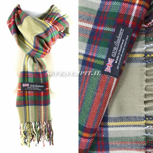 A plaid scarf shown in a split view: on the left, the scarf is draped on a white background with fringe at the bottom and a sewn-in label reading '100% Cashmere' and 'Scotland Made'; on the right, a close-up shows the tartan pattern with red, green, blue, yellow, and beige stripes. A watermark 'SEVEN CAPITL.