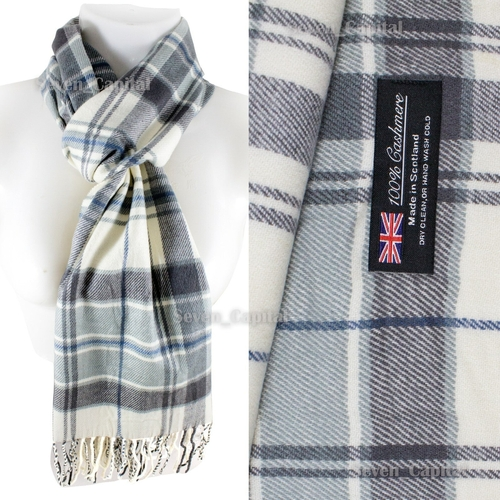 A plaid scarf in off-white, gray, and blue tones, shown draped on a white mannequin torso alongside a close-up of the fabric texture and a black brand label reading '100% Cashmere Made in Scotland'.