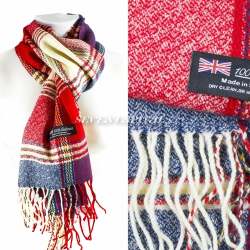 A multicolor plaid wool scarf with white fringe, shown draped on a white mannequin torso and in a close-up detail view. The scarf features red, navy blue, purple, and cream stripes in a tartan pattern, with a black woven label that reads '100% Made in UK'.