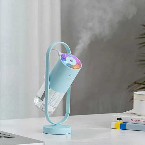 Blue humidifier emitting mist on a desk with books and a plant in the background