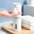 Hand holding a white foam soap dispenser with soap on a wooden tray.