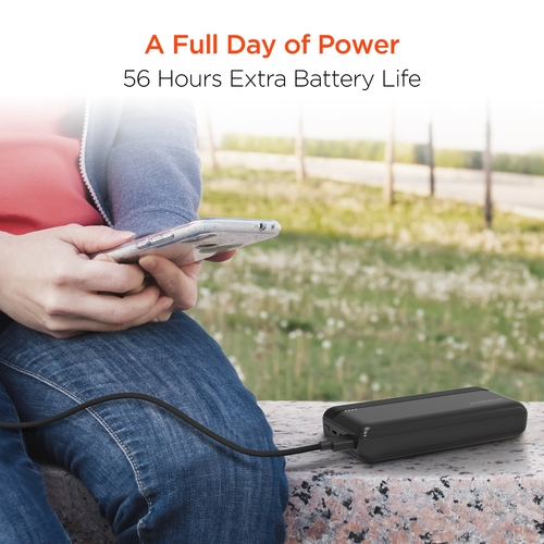 Person using a smartphone with an external battery pack in a park setting, emphasizing extended battery life.