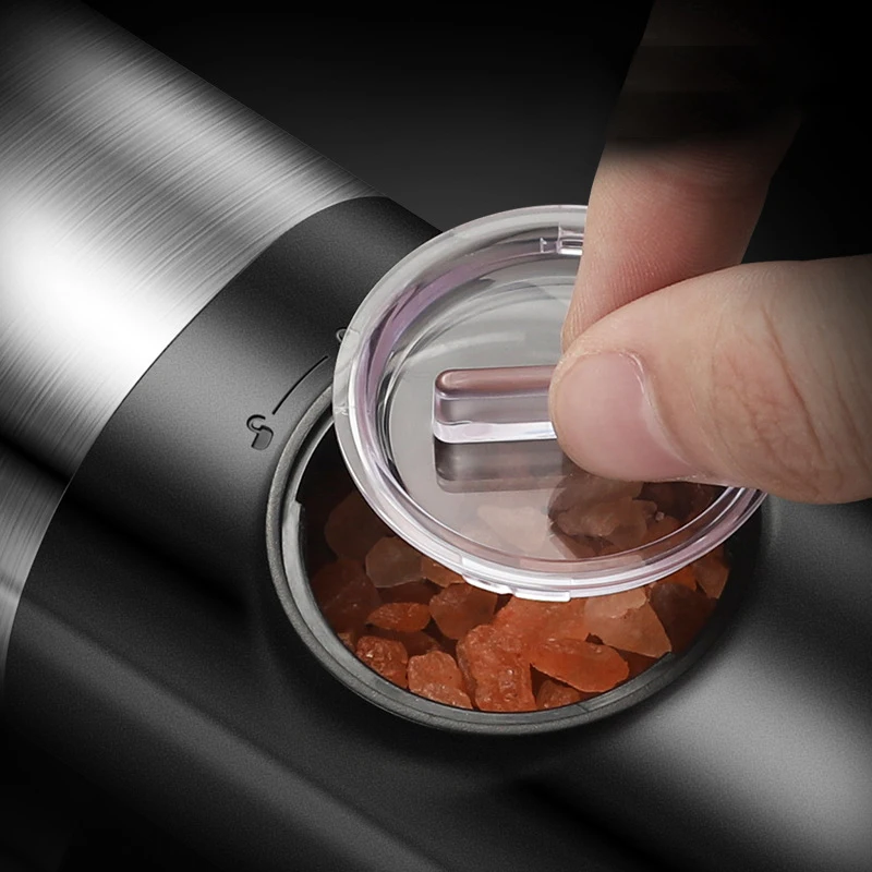 Close-up of a hand lifting a clear plastic lid from a black cylindrical container, showing orange-brown crystals inside.