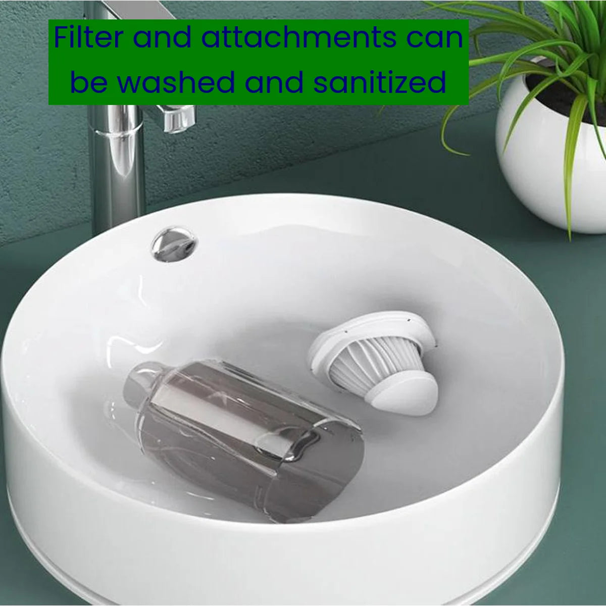 A white round bathroom sink filled with water, showing a dark gray filter cartridge and a white pleated filter element. A chrome faucet is visible, along with a green text banner at the top stating 'Filter and attachments can be washed and sanitized' and a potted plant in the upper right.