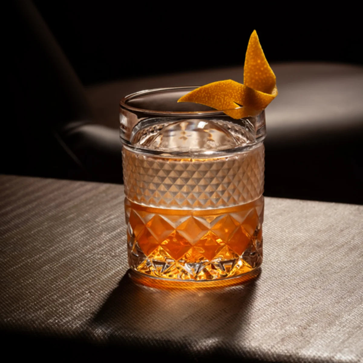 Glass tumbler with amber cocktail and an orange twist on a table