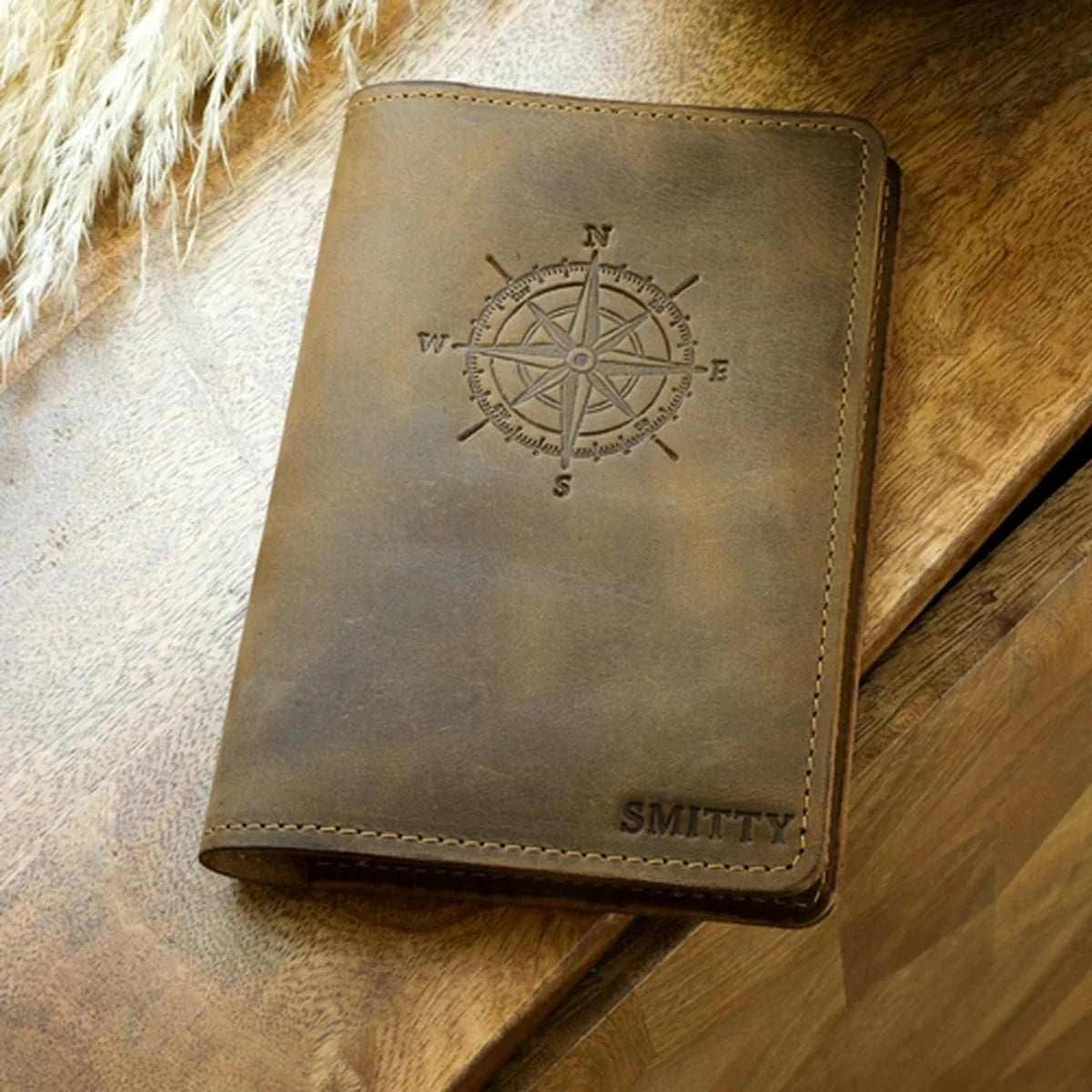 Brown leather notebook with compass design and 'SMITTY' branding on a wooden surface.