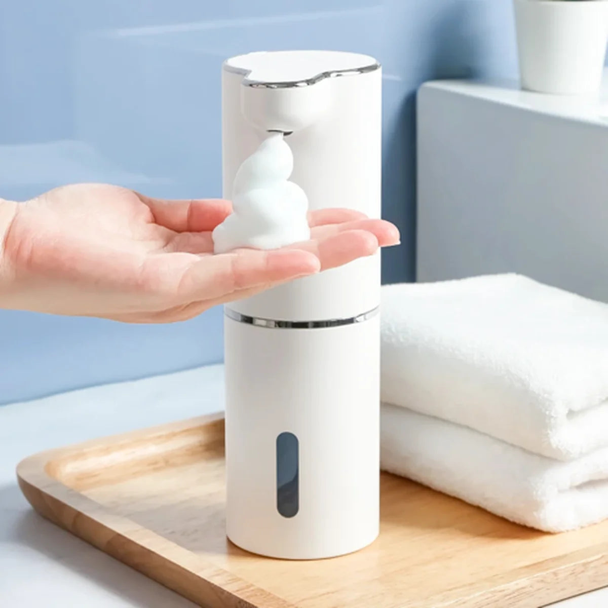 Hand holding a white foam soap dispenser with soap on a wooden tray.